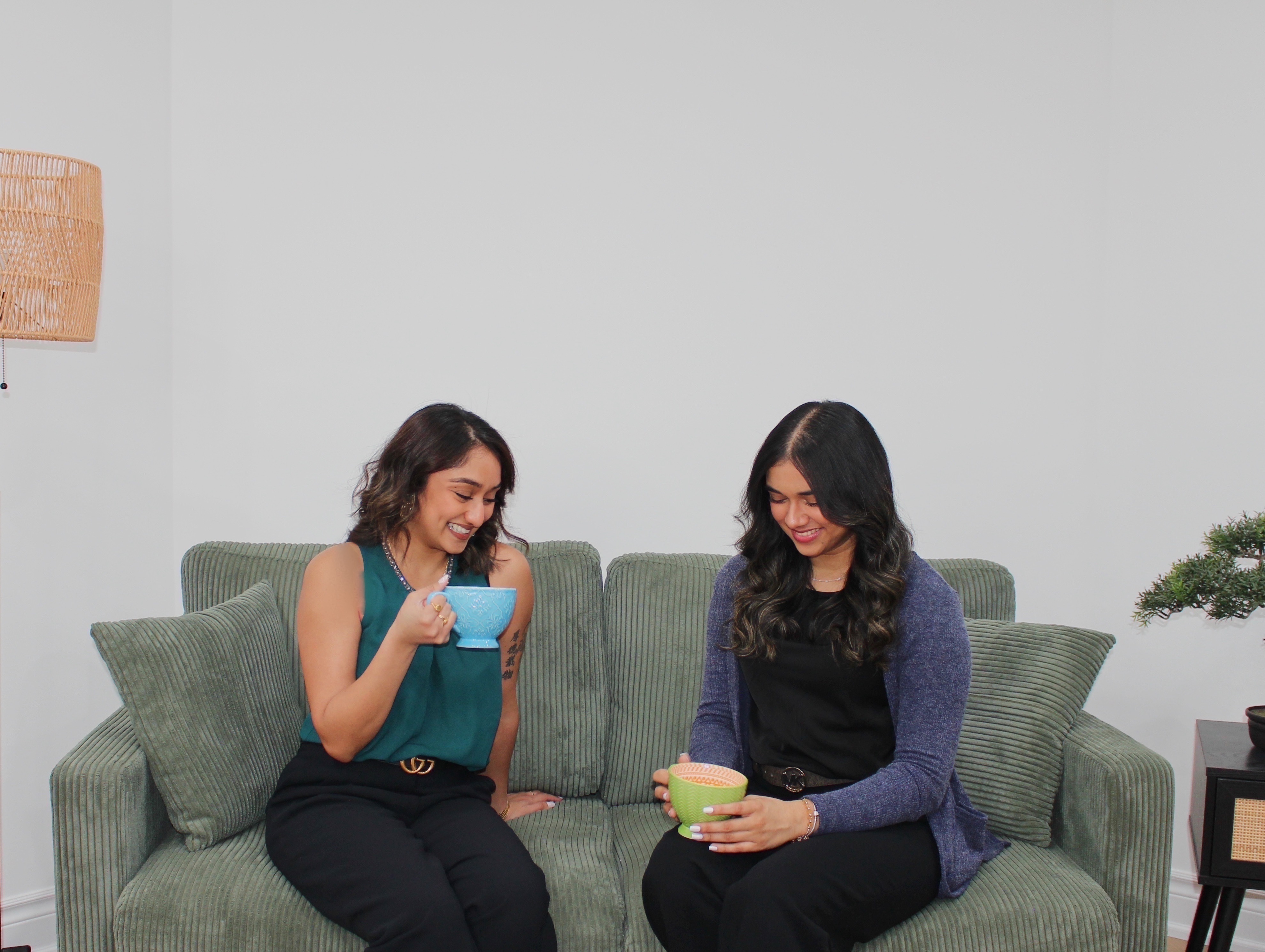 The two co-founders of Balance and Beyond relaxing on a couch with warm drinks beside a bonsai tree